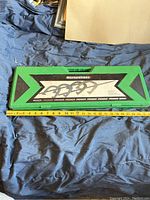 Closed green carrying case for horseshoes game with printed panel and handle, measure tape showing approx 18 inches length.