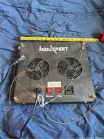 Back view of InduXpert LED grow light with two cooling fans, power plug, hanging cables, and two red switches labeled Bloom and Veg with measuring tape showing approximate size.