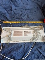 Back side of rectangular white indoor growing light fixture showing label, chains, and power cord laid out beside a tape measure.
