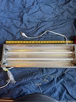 Top view of the rectangular metal light fixture showing two fluorescent tubes inside and a yellow measuring tape.