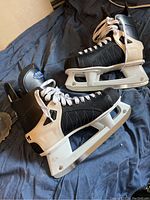 Side angle photo showing a pair of men's CCM ice hockey skates in size 11, black and white with white laces and white plastic blade holders.
