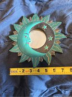 Top view of wooden decorative mirror shaped as a sun with a crescent moon inside, showing a ruler for size reference, measuring about 7 inches across.