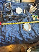 Photo showing overall lot contents including metal food presses, ladles, smoke detector, small bottle, mortar and pestle, wooden clothespin box and ceramic dish.