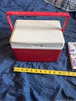 Closed small Coleman cooler with handle and measuring tape showing width approx. 10-11 inches.