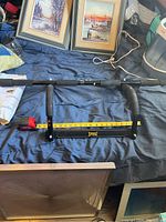 Everlast branded black metal doorway pull up bar with foam grips, placed on a bed, with tape measure showing length.