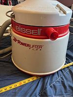 Front view of the main cylindrical unit showing Bissell and PowerLifter Plus branding and a red knob.