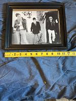 Framed black and white photo of ZZ Top with signatures of the band members visible. The photo is placed on a cloth with a measuring tape showing approximately 11 inches width.