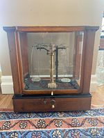Front view of the antique Chainomatic scale enclosed in a wooden and glass case.
