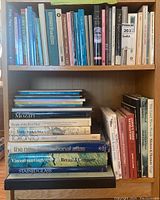 Photo showing two shelves with multiple hardcover and softcover books of various topics and colors, some stacked horizontally and others vertically.
