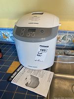 Closed bread maker unit on countertop next to user manual.