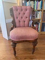 Front view of wooden framed chair with dusty rose tufted upholstered back and seat, carved legs and casters.