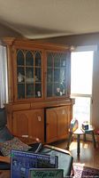Full view of antique pine corner china cabinet showing upper glass doors, lower wood doors, surrounding room context.