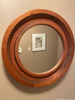 Circular mirror with thick reddish wooden frame hanging on beige wall with visible natural wood grain and dark marks.