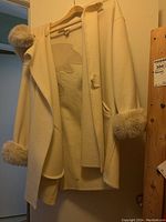 Front view of wool coat hanging on wooden hanger showing attached hood and fur-trimmed cuffs