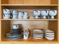 Overall view of two wooden shelves holding all pieces: mugs, footed cups atop, plates and bowls below