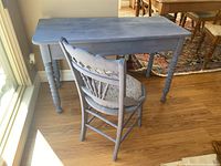 Blue-grey painted wooden desk and matching chair against a wall with sunlight from window