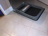 Side angle view of folded platform hand truck dolly on tiled floor showing metal frame and black platform surface