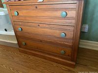 Front view of a wooden dresser with three drawers and green circular knobs showing some wear.