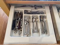 Flatware knives, forks, spoons arranged neatly in a kitchen drawer organizer with white plastic dividers.