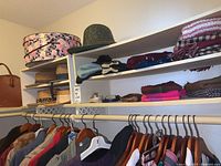 Three shelves with assorted hats, gloves, scarves, and belts above hanging clothes.