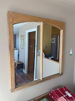 Front view showing the large square mirror with two vertical mirror panes separated by wooden frame, reflecting room interiors.