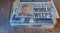 Stack of several vintage newspapers with one showing headline 'World Weeps' featuring John F. Kennedy photo dated Nov 23, 1963.