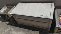 Suncoast resin patio box shown outdoors with a hinged lid closed, dirt and weathering visible on surfaces.
