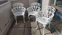 Three white metal patio chairs arranged on a balcony floor