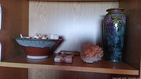 Shelf showing the Royal Doulton vase with grape motif, pottery bowl, cross stitch wall hanging, and natural coral piece.
