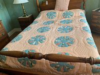 Full view of the quilt on a wooden four-poster bed showing the circular blue floral appliqué and peach background with quilted texture.