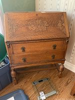 Front view of oak secretary desk showing carved floral inlay on fall-front and two drawers below