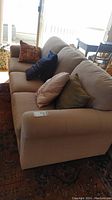 Full side view of beige upholstered sofa with various colored pillows on it.