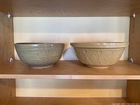 Pair of stoneware bowls on wooden shelf showing size and color difference.