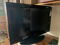 Front view of Toshiba 32-inch flat screen TV showing black glossy bezel and pedestal stand on wooden surface.