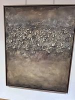 Full view of the abstract artwork showing raised textured central pattern on a dark metallic swirled background, framed in gold.