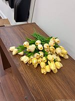 A bunch of yellow artificial tulips placed on a wooden surface, showing multiple flower buds and green stems.