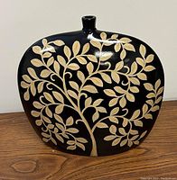 Front view of black ceramic vase showing gold leaf and branch pattern against a smooth black background, placed on wooden surface.