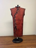 Full view of the tall red geisha dress metal sculpture mounted on black oval base, showing the overall shape and color.