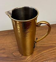 Side angled view of tall gold hammered pitcher showing handle and spout.