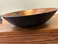 Side view of the hammered copper bowl showing the shallow curve, black exterior, and copper interior.