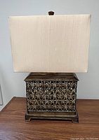 Front view of bronze metal base lamp with creamy tan rectangular shade showing ornate detail on base and shape of shade.