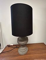 Front view of the lamp showing the textured gray resin base and tall black fabric shade on a wooden surface.