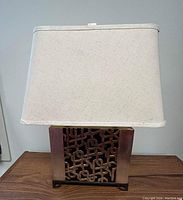 Front of the lamp showing white fabric shade and black metal base with decorative gold leaf patina panel.