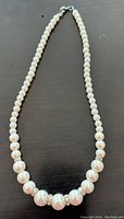 Full view of pearl necklace laid flat showing length and arrangement of pearls and cubic zirconia spacers.