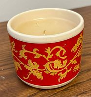 Front side view of the red ceramic candle holder with gold leaf design showing the ornate pattern.