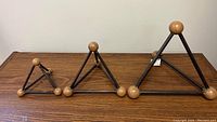 Set of three iron triangle sculptures with wooden spherical joints, arranged in order from small to large on a wood grain table surface.