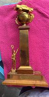 Front view of the race car trophy showing the wooden base with a man figure holding a trophy on the side and a tall wood column topped with a brass cup and classic race car model.