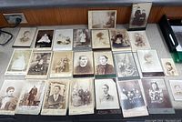 Wide view photo showing all 25 antique photos arranged on a table featuring portraits of various individuals from early 1900s.