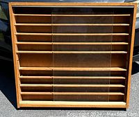 Front view of the wooden display cabinet showing nine shelves and two sliding glass doors, one glass panel broken.