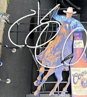 Full view of neon advertising sign showing cowboy on horse, neon tubing, and Coors beer bottle shaped sign mounted on black metal frame.